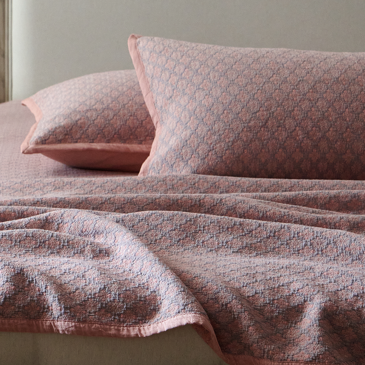 Close-up of layered dusty rose textured pillow shams on a cozy, lived-in bed.