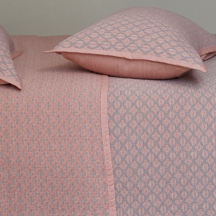 Top-down view of a dusty rose diamond jacquard pillow sham resting on the matching textured coverlet.
