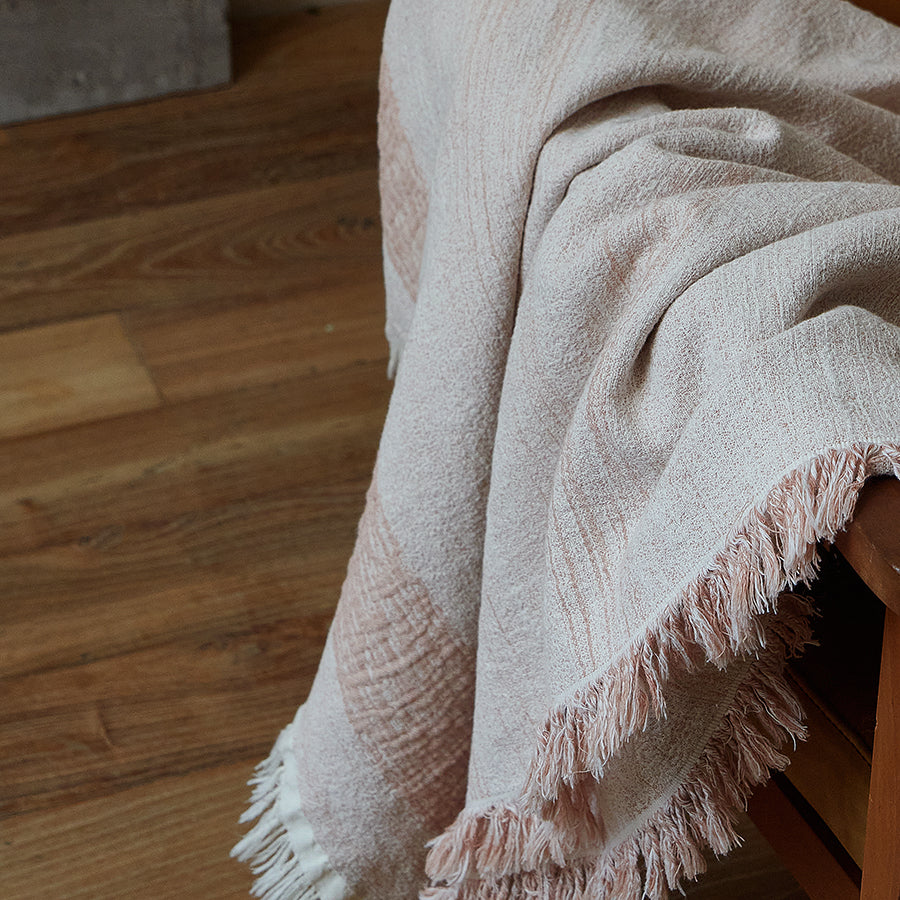 Dusty rose textured throw blanket draped elegantly, showing the natural fabric folds and fringe.