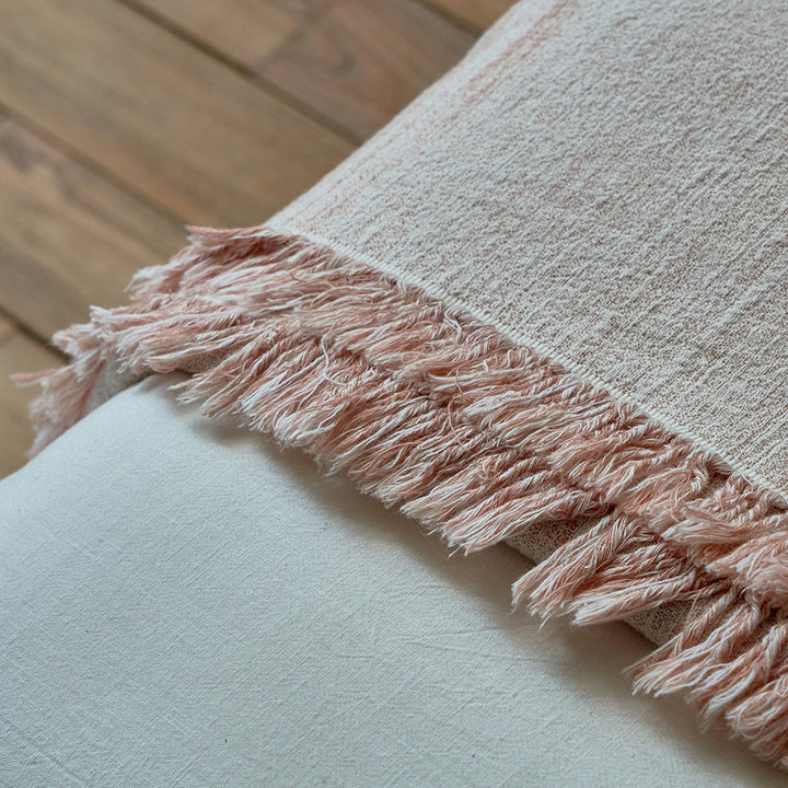 Macro shot of the fringe detailing on the dusty rose linen blend blanket over white bedding.
