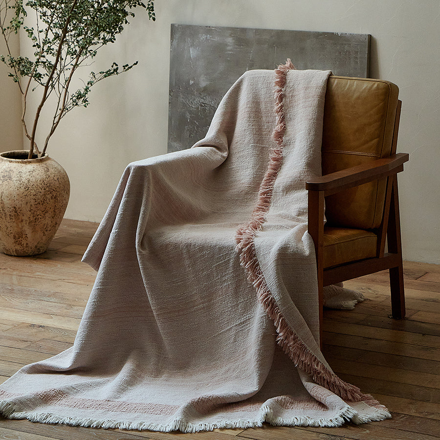 Dusty rose cotton-linen throw blanket gracefully draped over a reading chair.