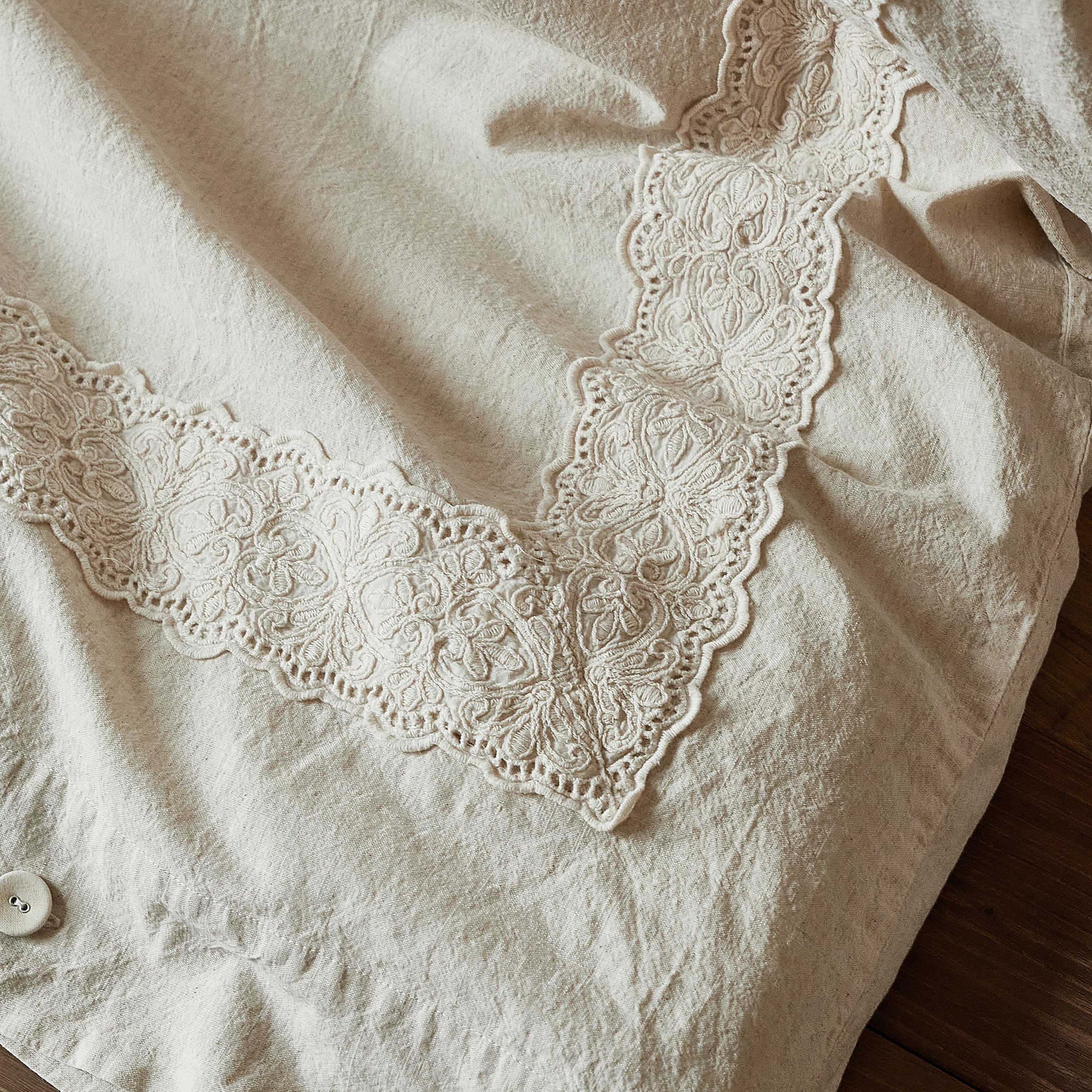 Detail of the intricate V-shaped 3D floral lace embroidery on the natural oatmeal duvet cover.