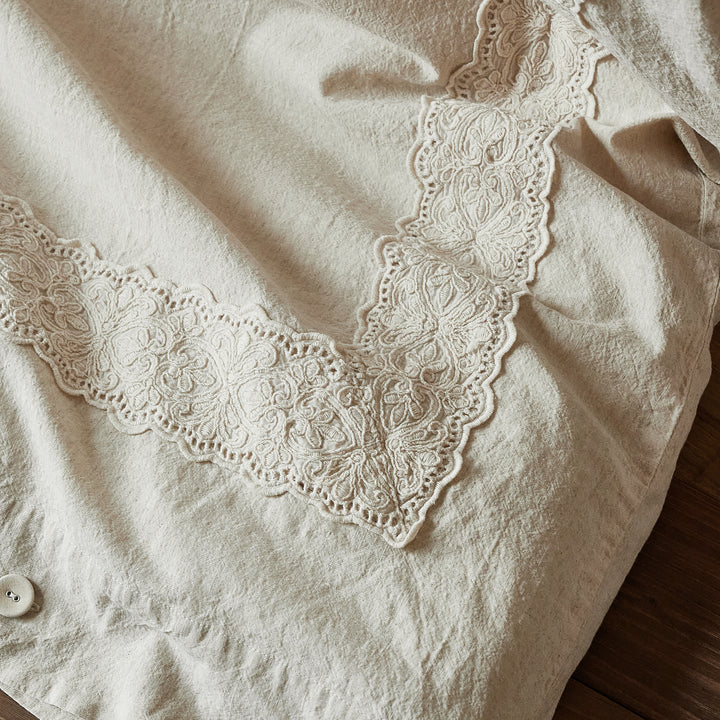 Detail of the intricate V-shaped 3D floral lace embroidery on the natural oatmeal duvet cover.