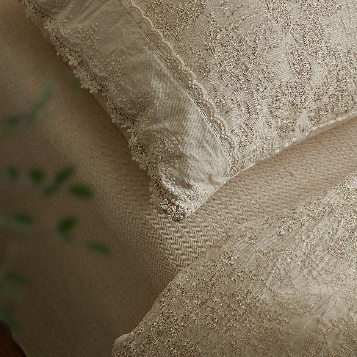 Close-up of floral jacquard weaving and scalloped lace trim on a warm beige cotton-linen pillow sham.