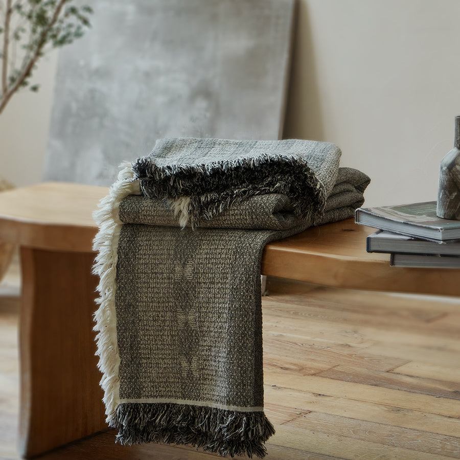 Neatly folded charcoal black summer throw blanket resting on a modern rustic wooden bench.