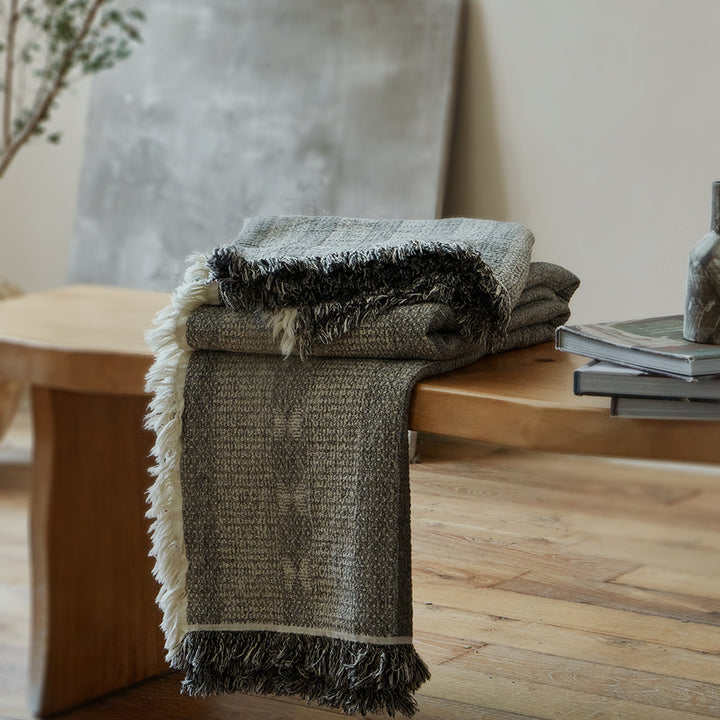 Neatly folded charcoal black summer throw blanket resting on a modern rustic wooden bench.