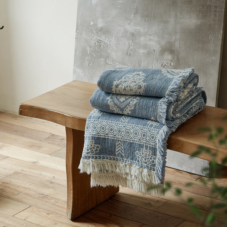 Neatly folded dusty blue summer throw blanket resting on a rustic wooden bench.