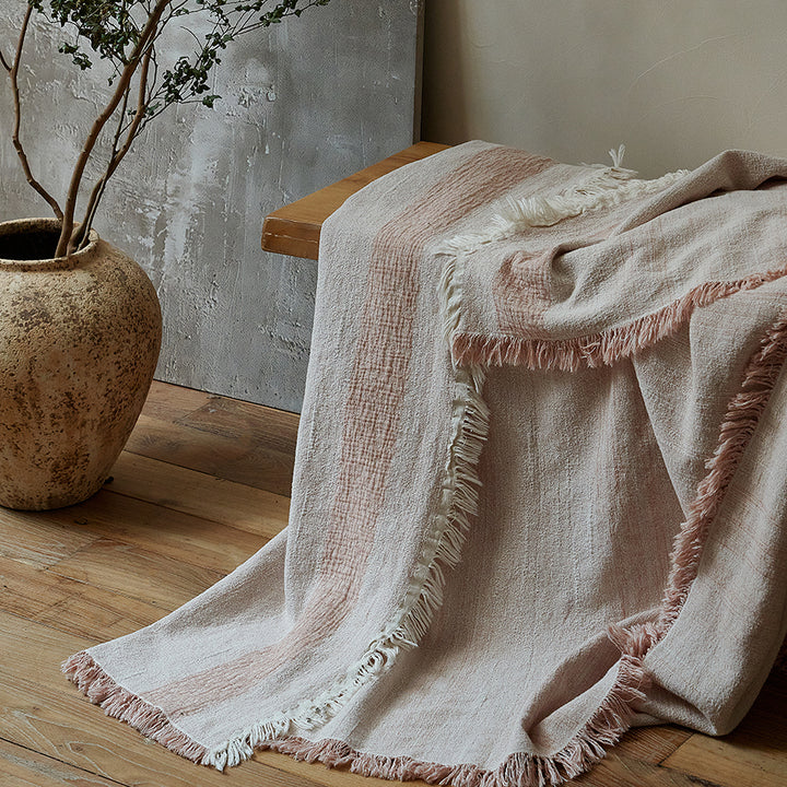 Neatly folded dusty rose summer throw blanket resting on a rustic wooden bench.