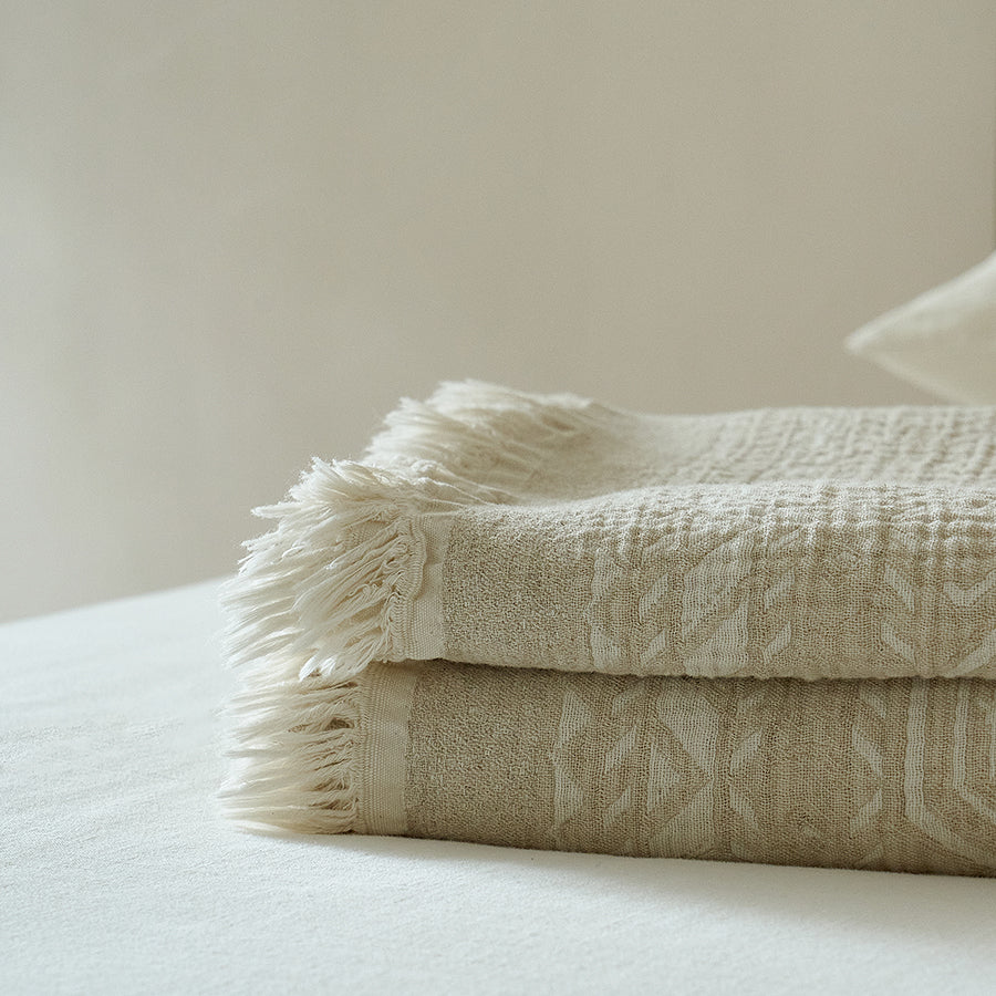 Folded oatmeal beige jacquard throw showing the precise woven edge design and fringes.