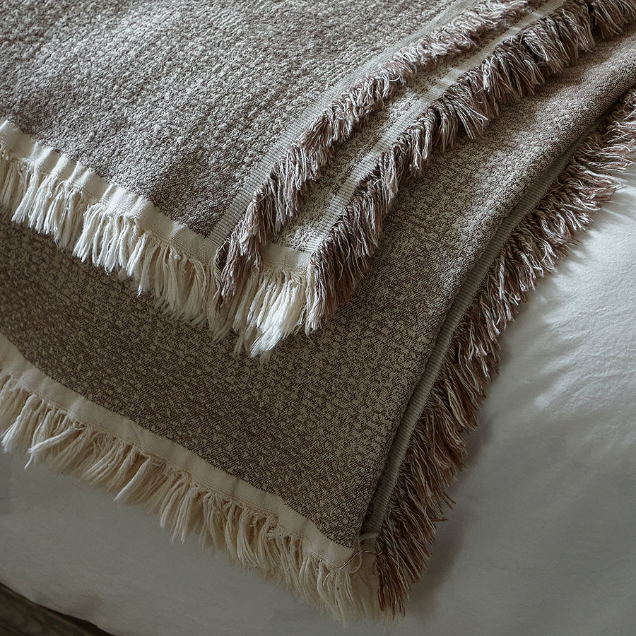 Folded taupe brown textured throw blanket showing the striped fabric and fringe edges.