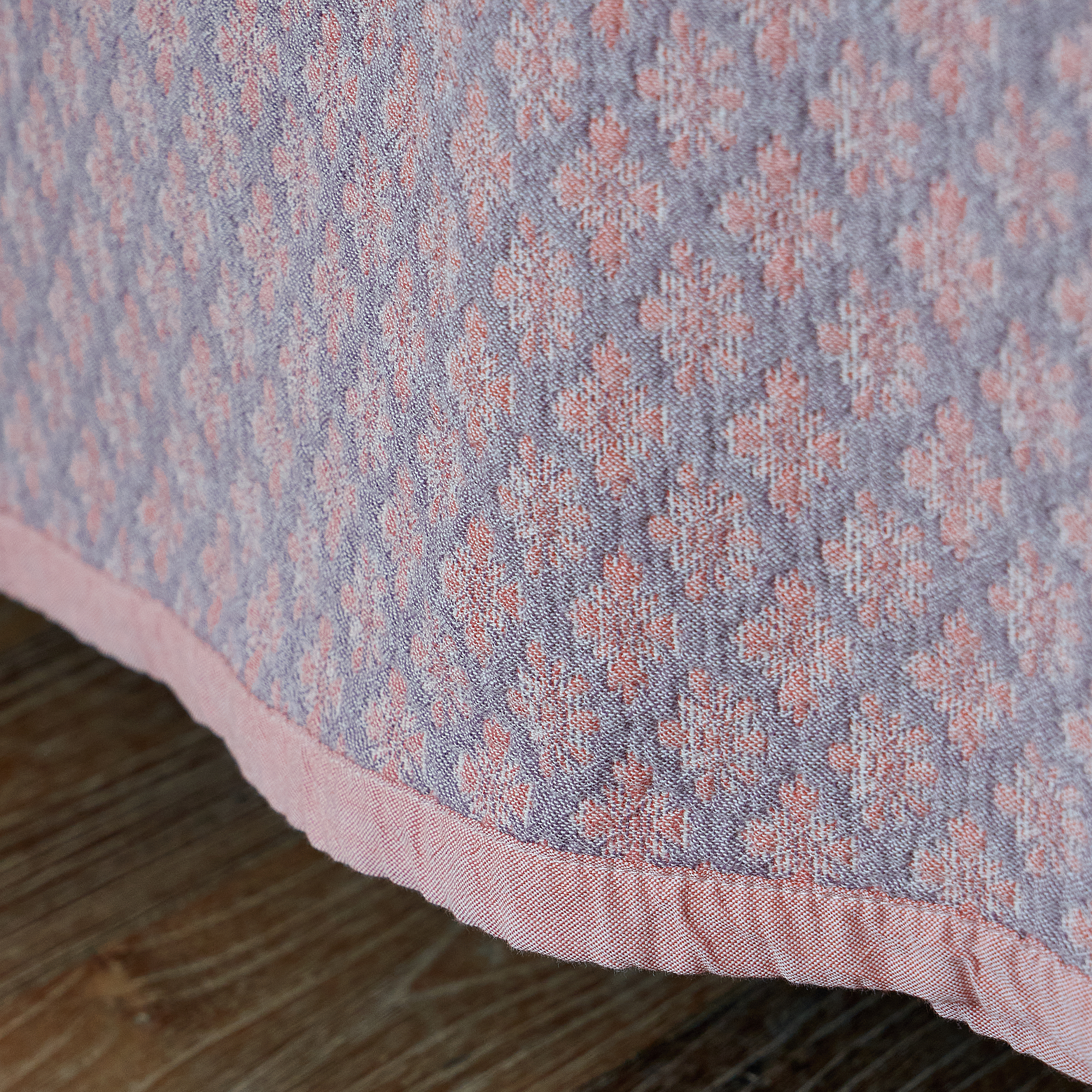 Beautiful drape of the dusty rose washed cotton coverlet cascading over the edge of the bed onto a wooden floor.