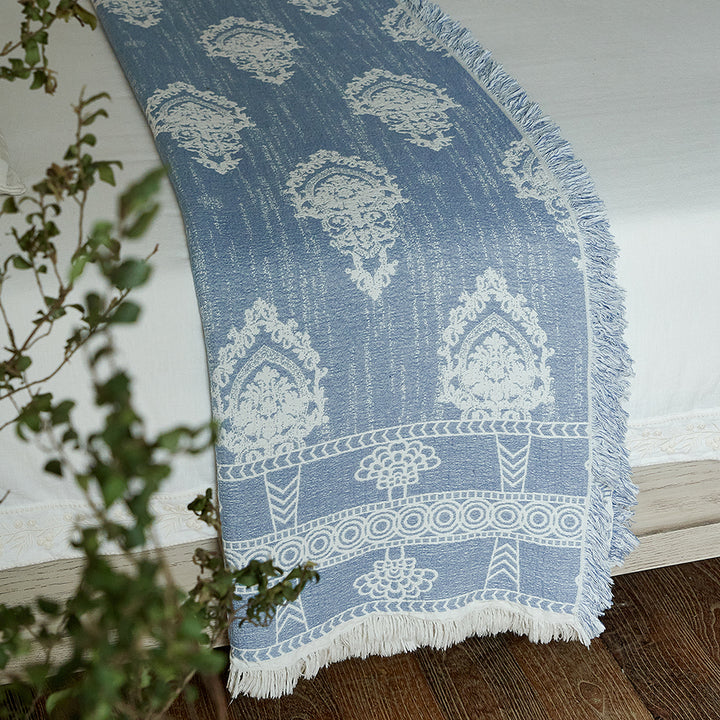 Dusty blue jacquard woven throw blanket hanging gracefully off the edge of a bed.
