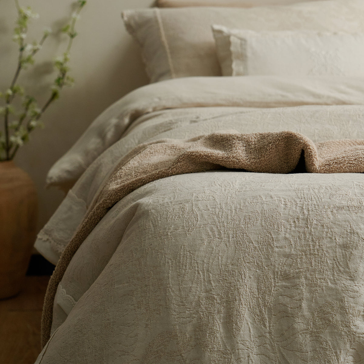 Close-up of textured botanical jacquard bedding with a natural beige throw draped across the bed.