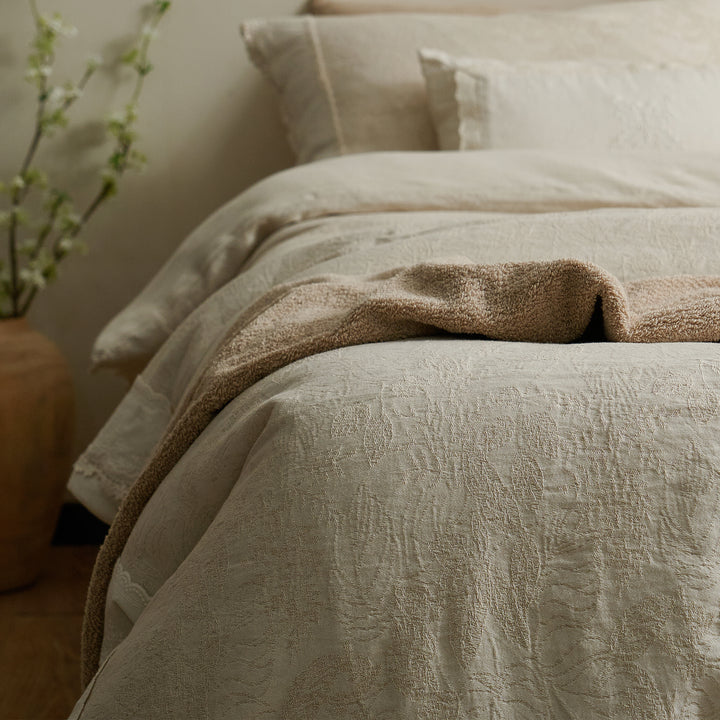 Close-up of textured botanical jacquard bedding with a natural beige throw draped across the bed.