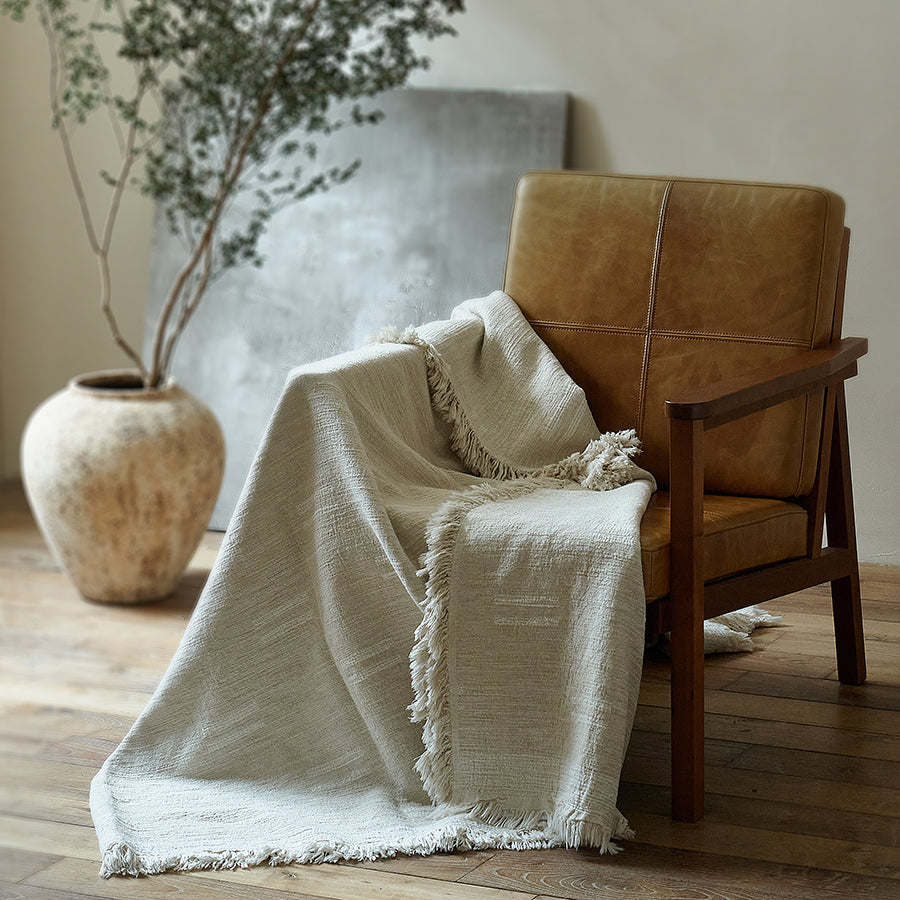 Light greige cotton-linen blanket casually draped over a brown leather armchair in a modern rustic room.