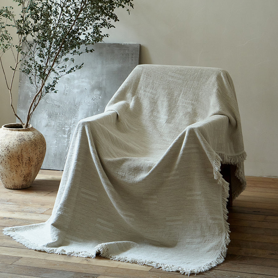 Light greige cotton-linen jacquard throw blanket gracefully draped entirely over a cozy reading chair.