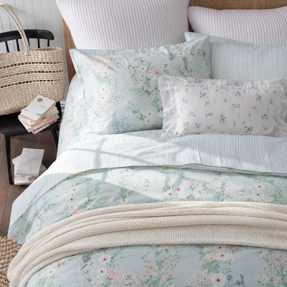 Side angle of a bed dressed in DAUAOTO mint breeze floral bedding, next to a rustic wooden nightstand and a woven basket.
