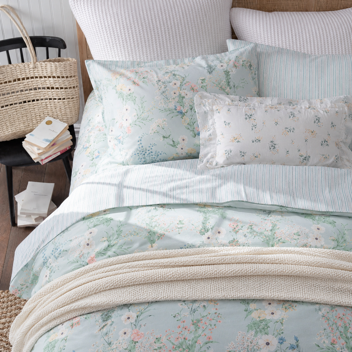 Side angle of a bed dressed in DAUAOTO mint breeze floral bedding, next to a rustic wooden nightstand and a woven basket.