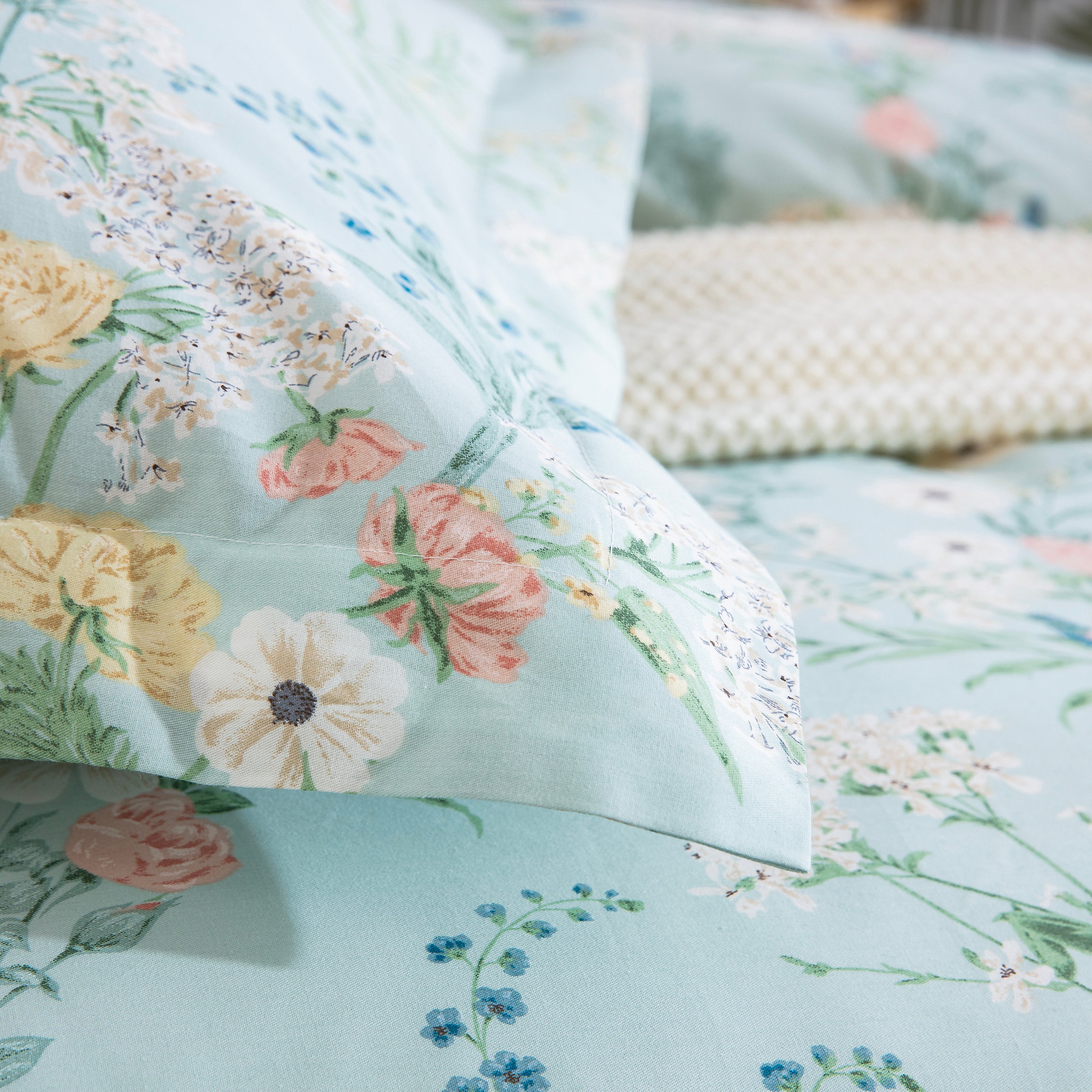 Close-up of stacked pillows showing the DAUAOTO mint floral pillowcases paired with subtle blue striped bed sheets.