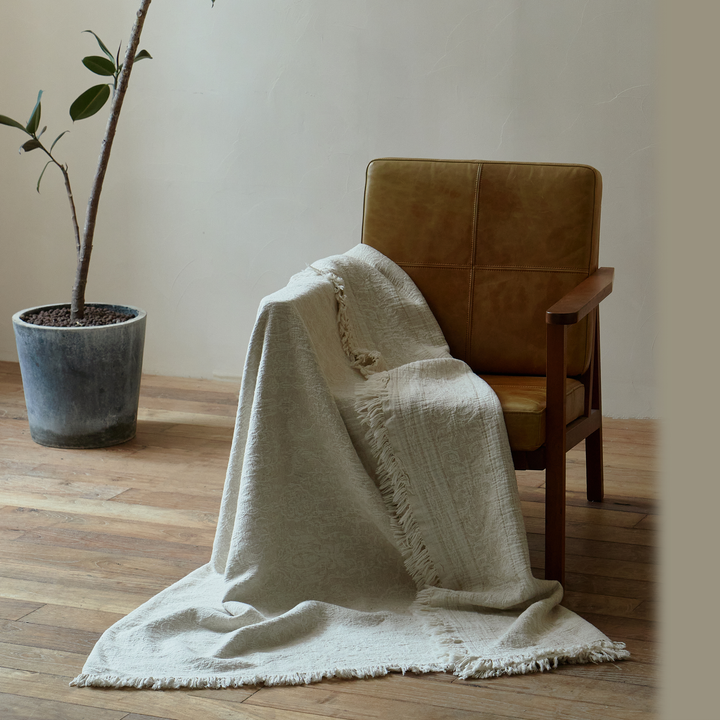 throw-draped-reading-chair.jpg	Natural ivory jacquard throw draped over a reading chair, showing the elegant fabric flow to the floor.