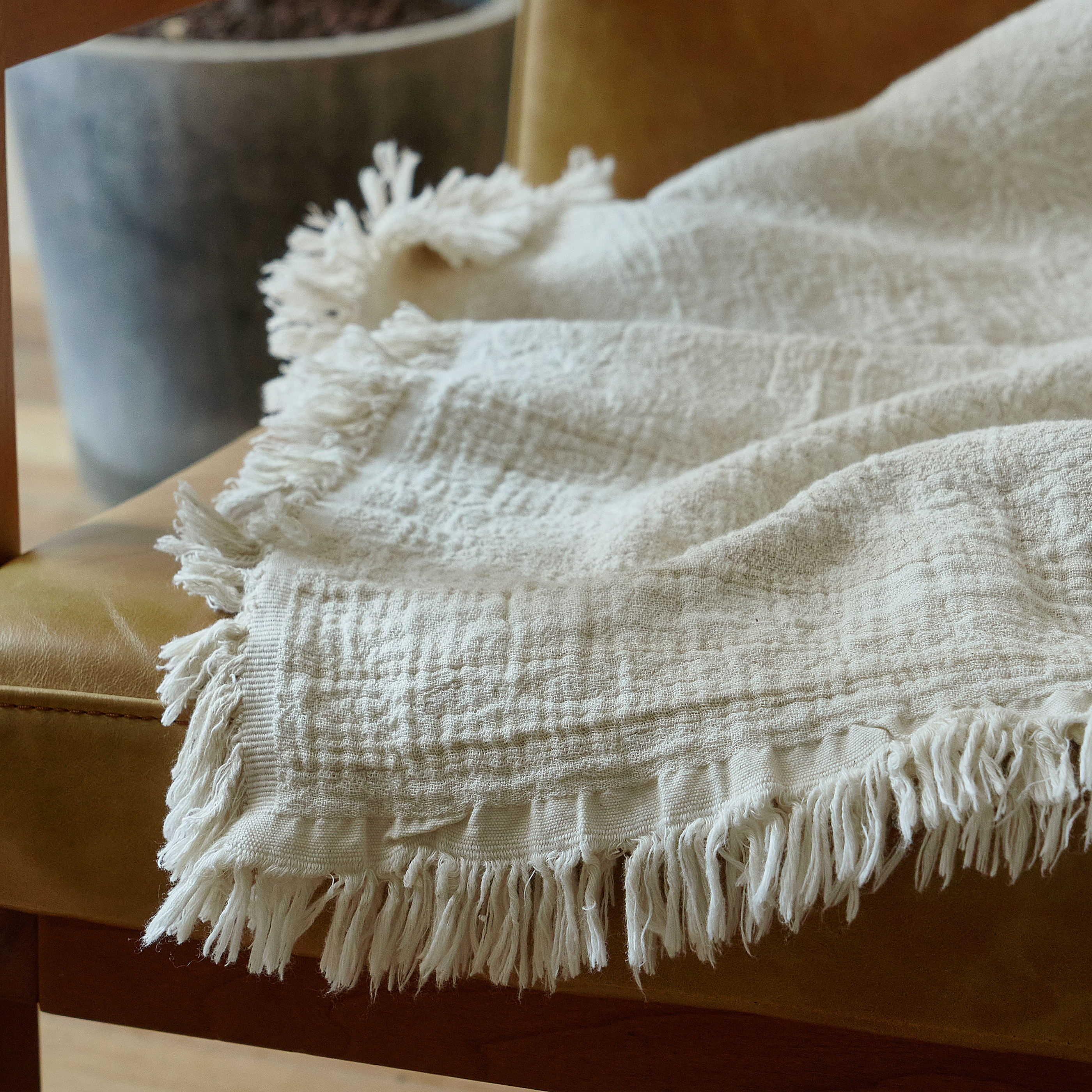 Close-up of the delicate fringed edge on a natural ivory cotton-linen throw resting on a chair arm.