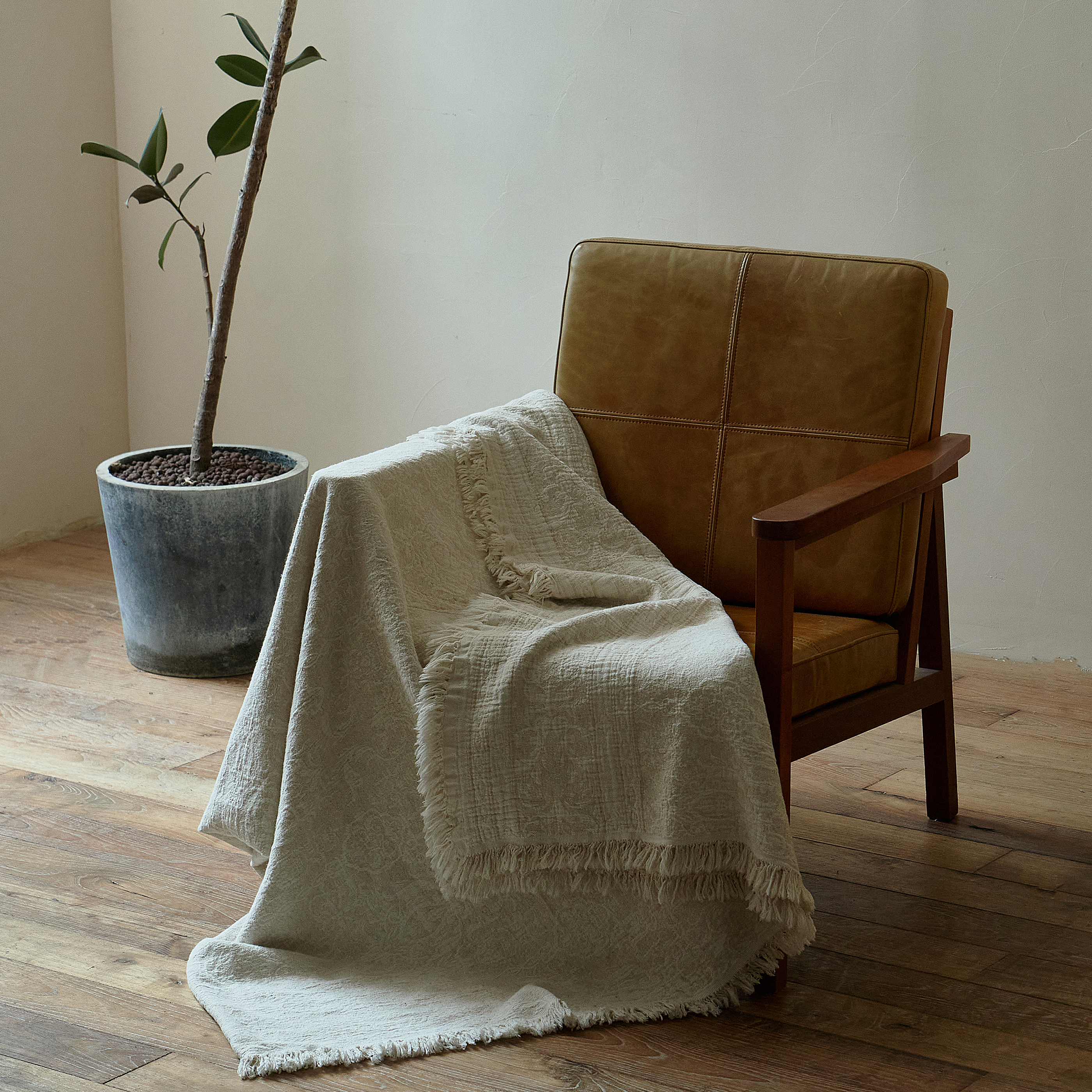 Natural ivory cotton-linen throw blanket gracefully draped over a brown leather armchair.