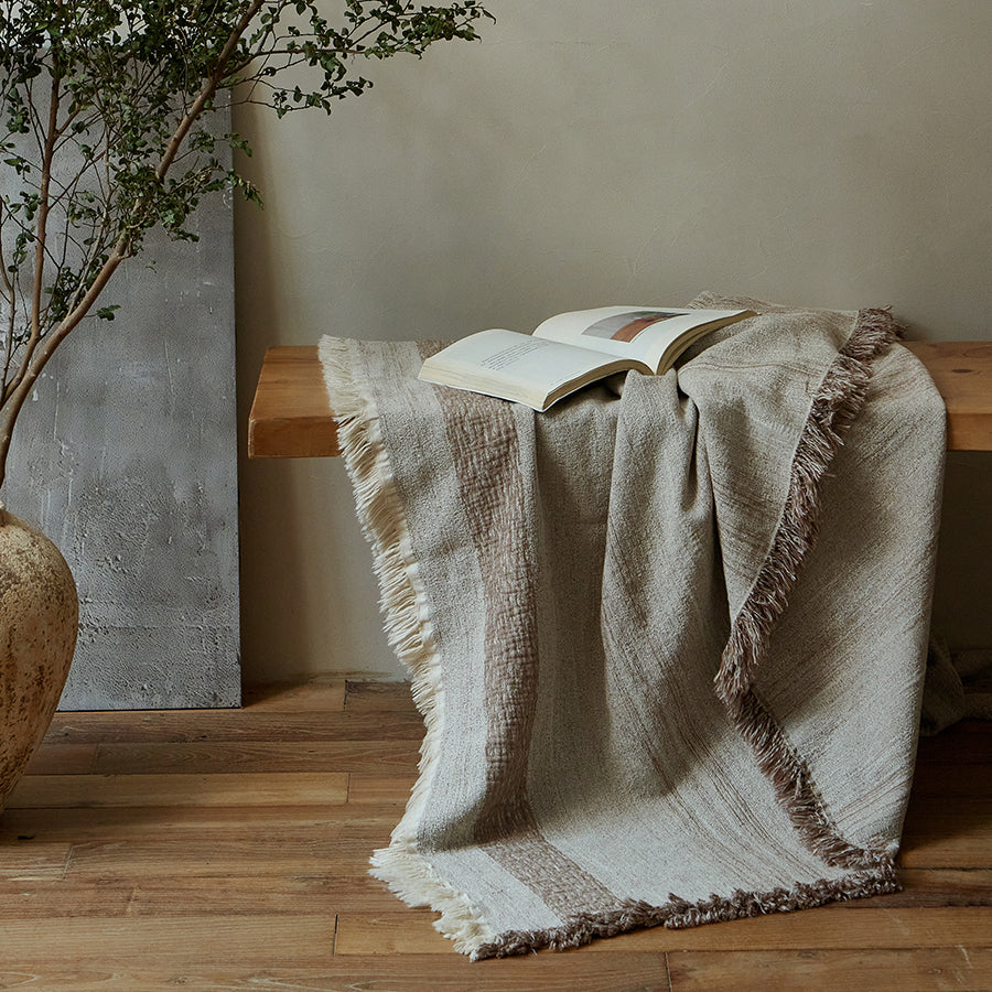 Warm sand rustic beige throw blanket elegantly draped over a wooden bench.