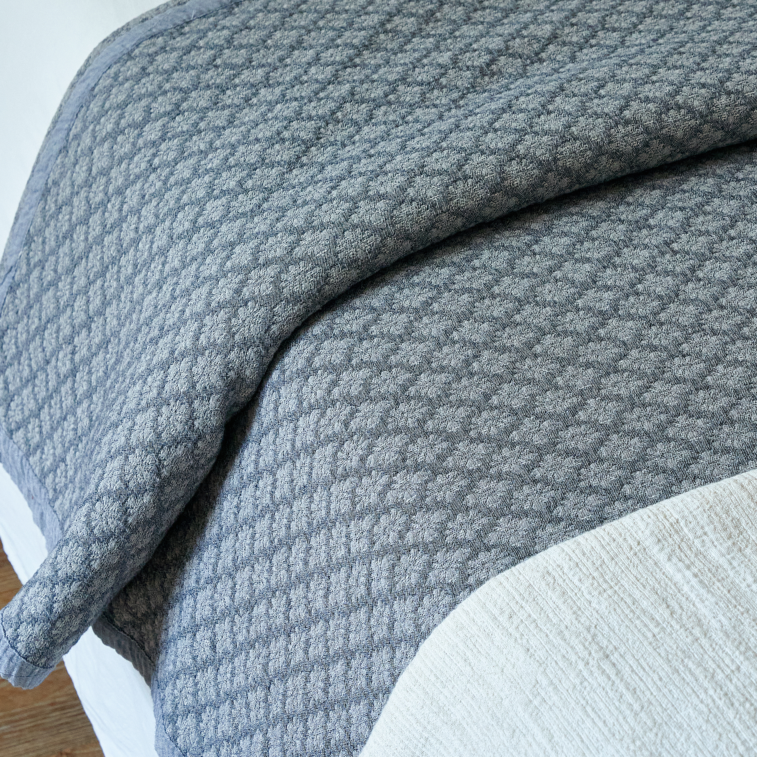 Folded edge of the slate blue jacquard coverlet revealing crisp white sheets underneath.