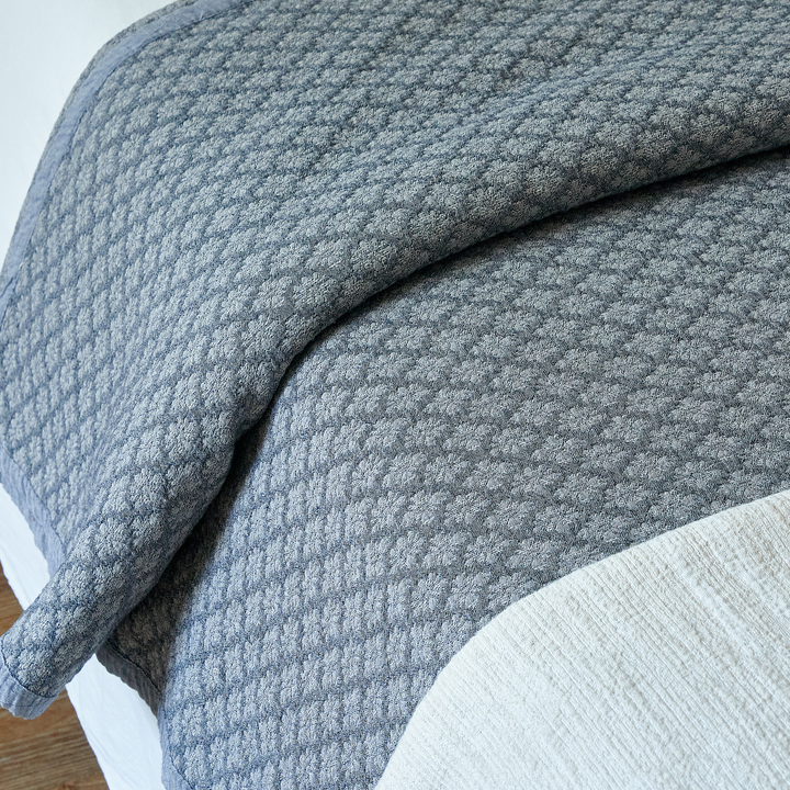 Folded edge of the slate blue jacquard coverlet revealing crisp white sheets underneath.