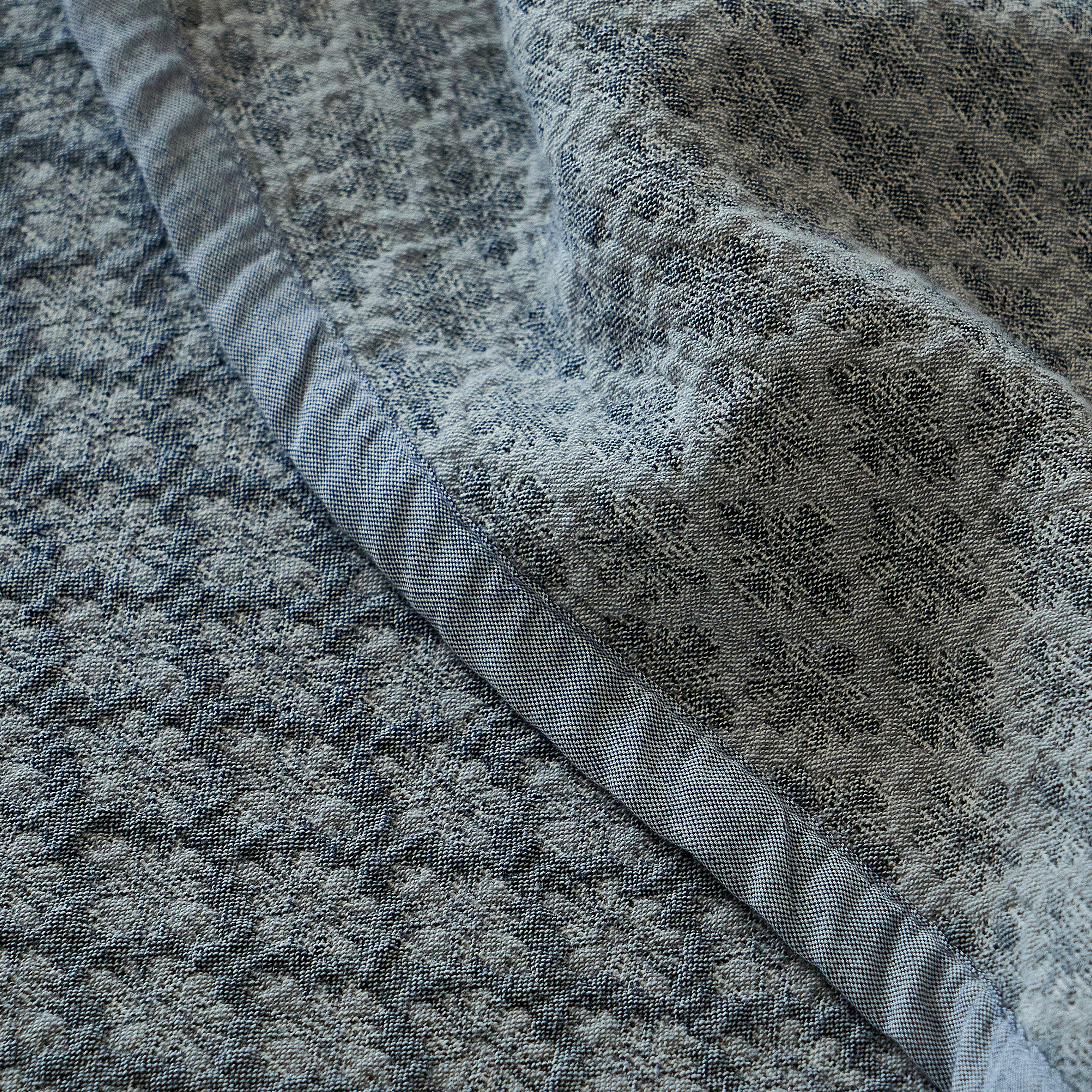 Macro detail of the narrow bound edge and woven texture on the slate blue cotton coverlet.