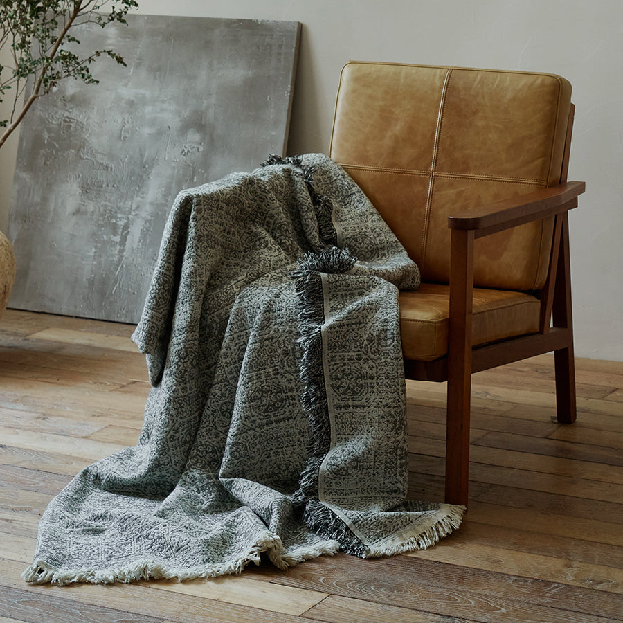 Slate grey vintage style cotton-linen blanket casually draped over a brown leather armchair.