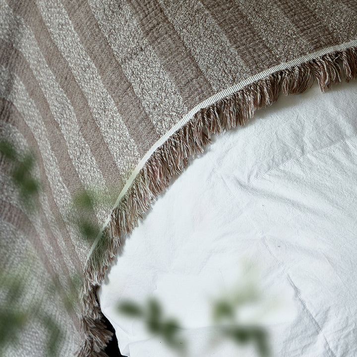 Detailed view of the striped fabric and natural folds on the taupe brown linen blanket.