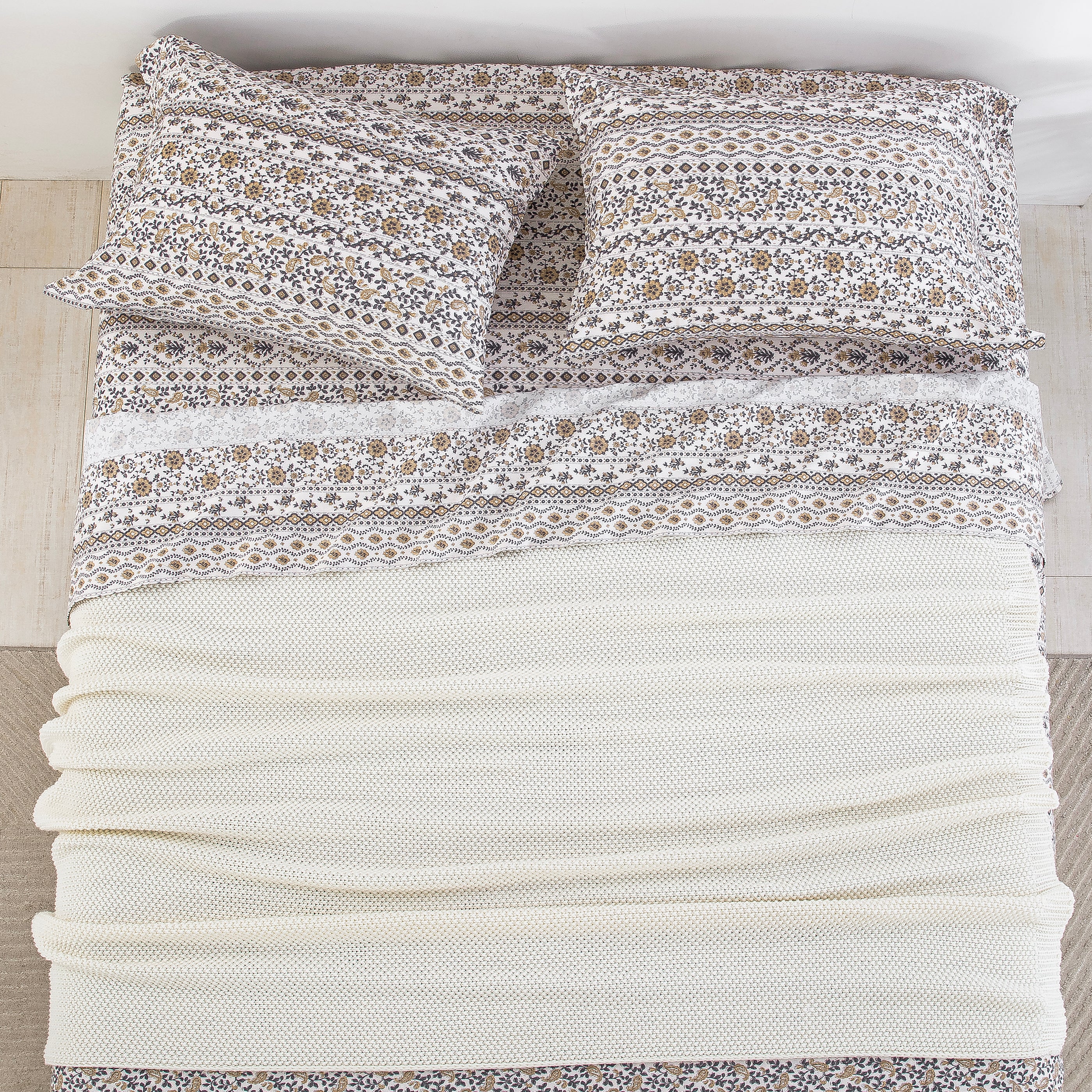 Top-down bird's-eye view of a neatly made bed featuring the DAUAOTO earthy block print sheet set layered with a cream blanket.
