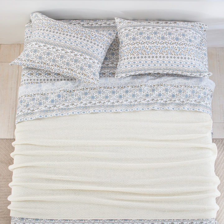 Top-down bird's-eye view of a neatly made bed featuring the DAUAOTO coastal blue block print sheet set layered with a cream blanket.