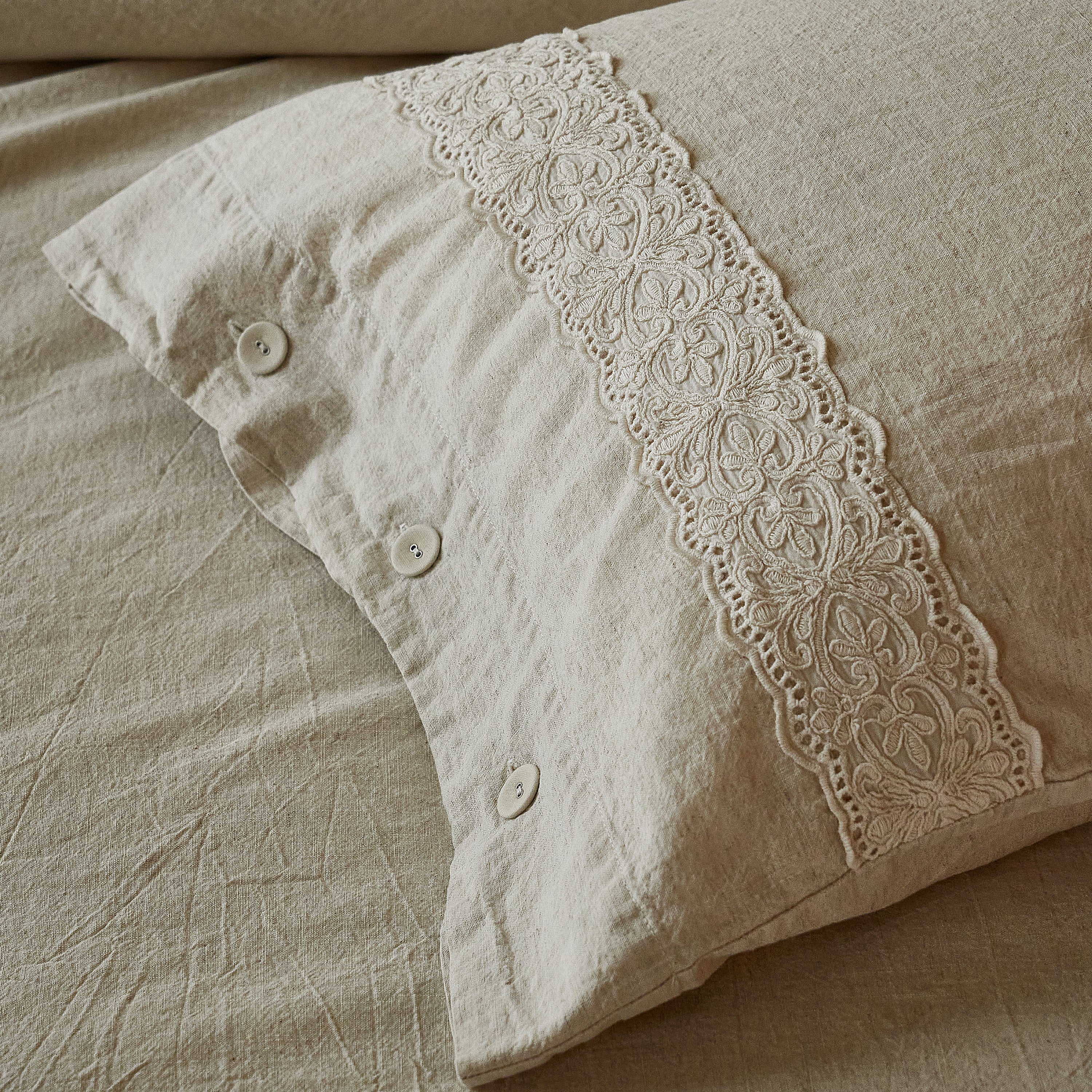 Side view of the oatmeal linen-cotton pillowcase featuring vintage French embroidered lace and natural buttons.