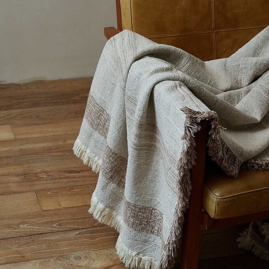 Detailed view of the contrasting stripe border and fringe on the warm sand linen blanket.