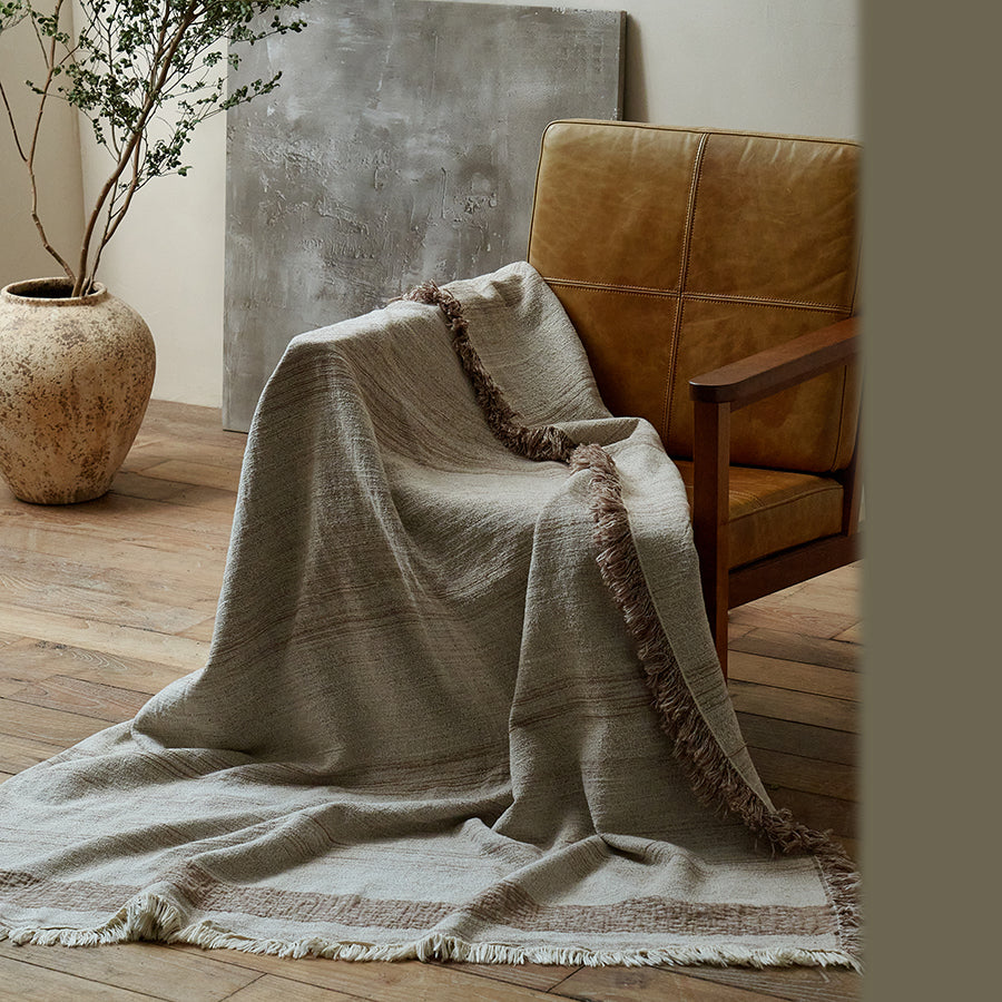 Warm sand cotton-linen blanket with contrasting border stripes draped over a leather chair.