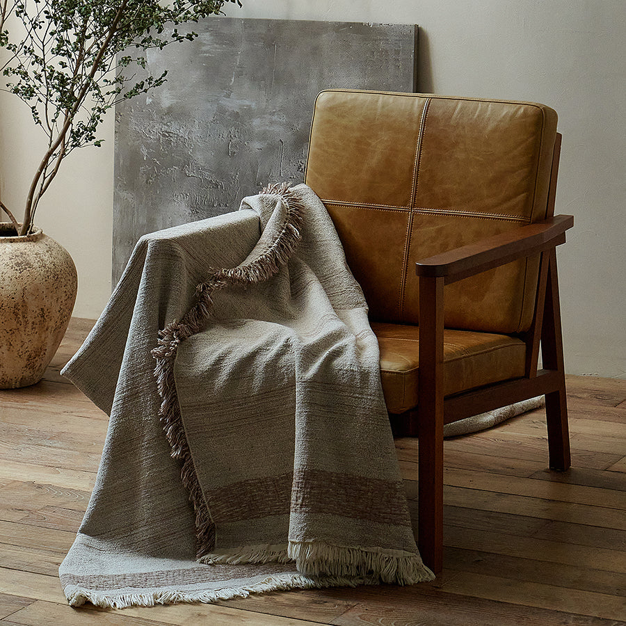 Warm sand cotton-linen jacquard throw blanket gracefully draped over a rustic reading chair.