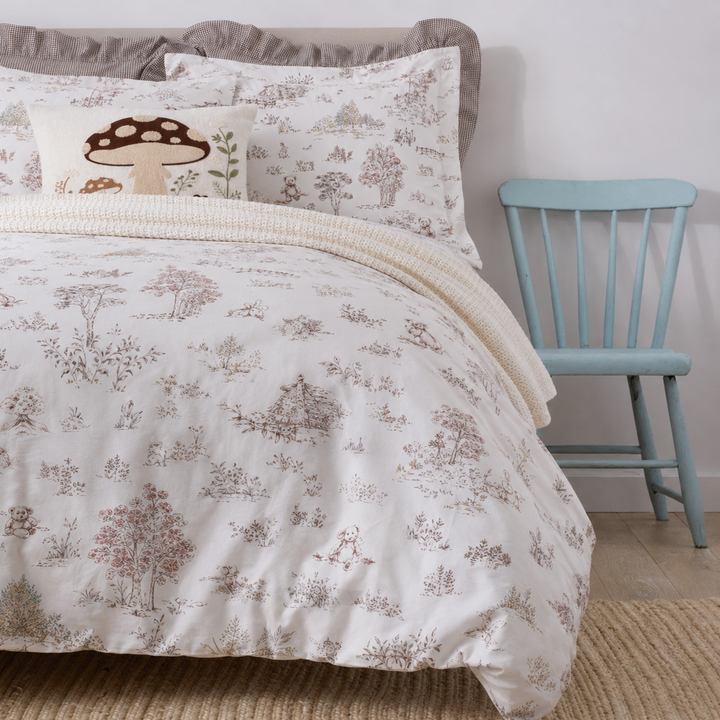 Side angle of a bed dressed in DAUAOTO vintage woodland cotton bedding next to a rustic light blue chair.